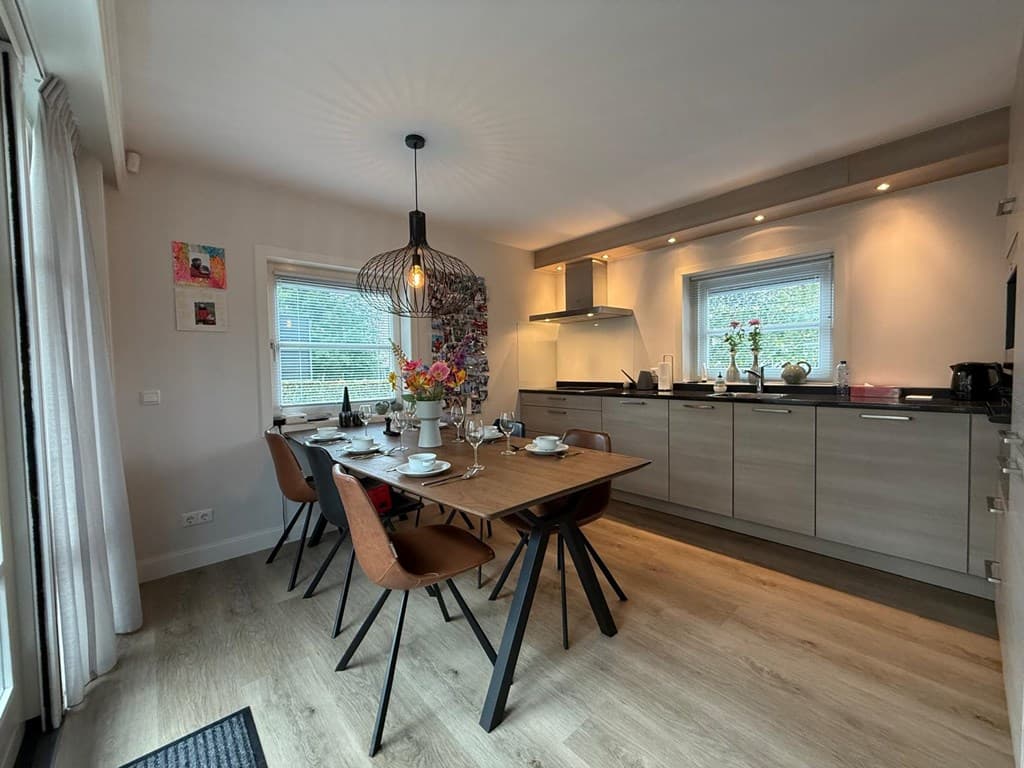 Eet- en keukenruimte met een houten eettafel, moderne meubels en een grote lamp boven de tafel.