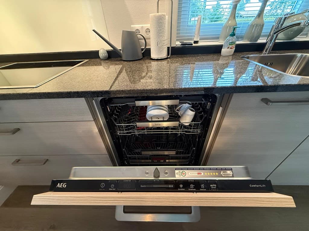 Inbouwvaatwasser met open lade en schone vaat in een moderne keuken met een zwarte granieten werkblad.