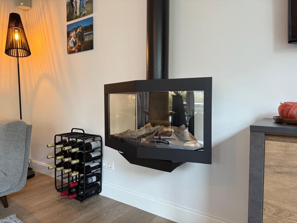 Moderne woonkamer met een hangende haard, wijnrek en sfeervolle lamp in een lichte interieur.
