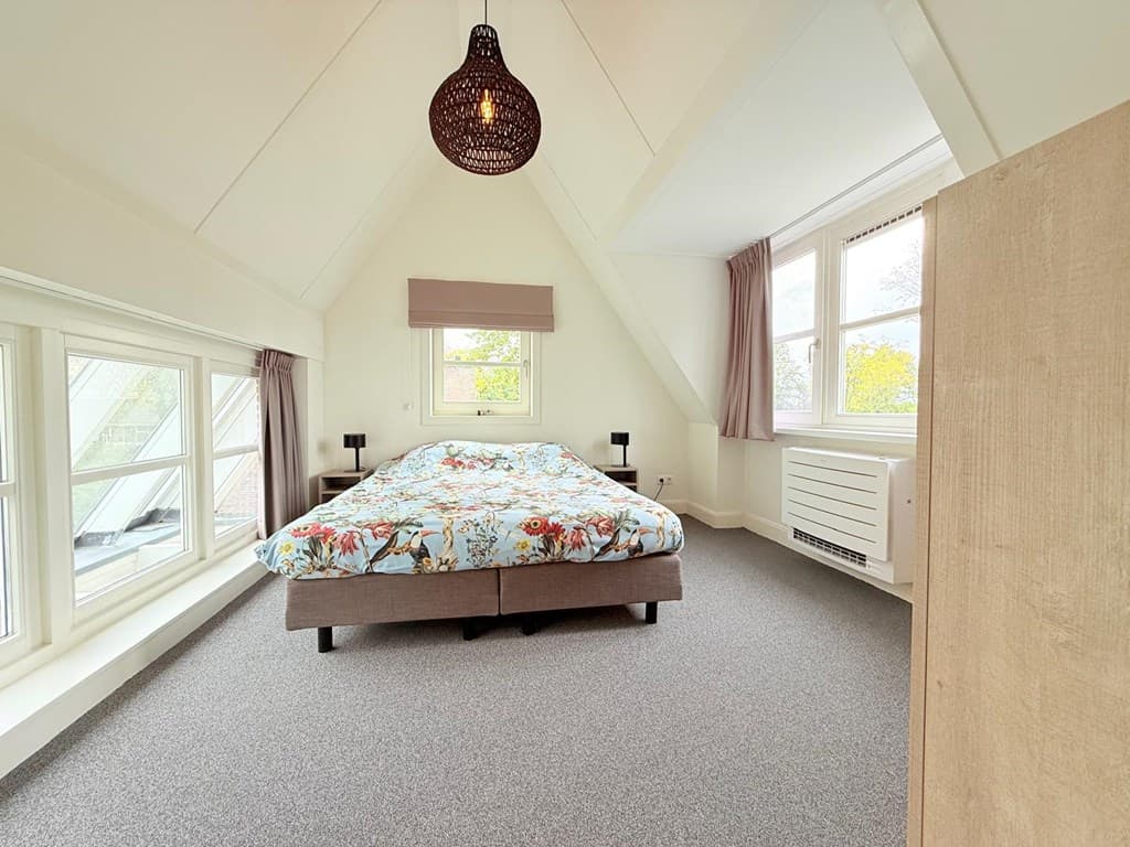 Sfeervolle slaapkamer met een groot bed, tapijt en ramen die zorgen voor veel natuurlijk licht
