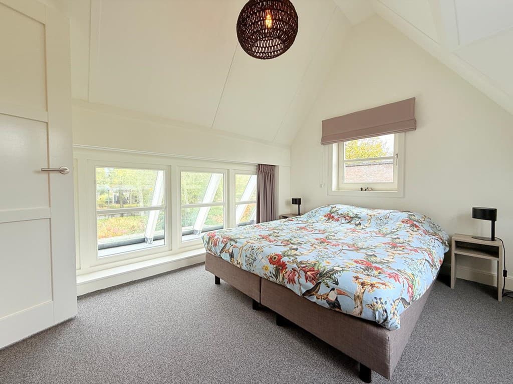 Slaapkamer met groot bed, raam met uitzicht, en een moderne inrichting met vloerkleed en nachtkastjes.