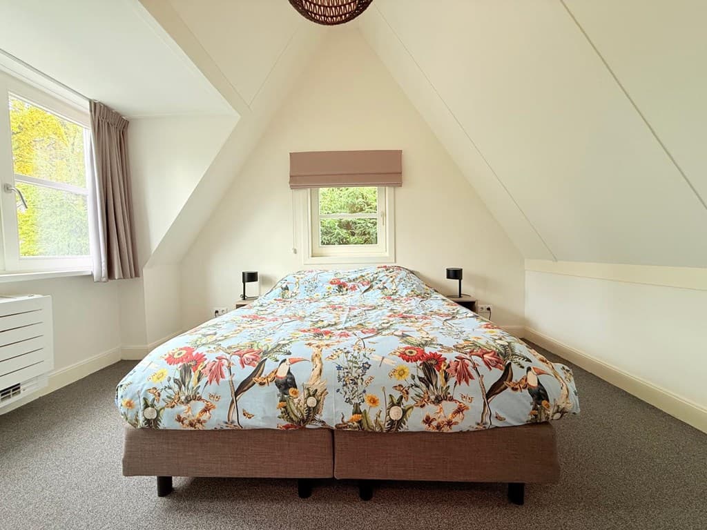 Slaapkamer met een groot bed, kleurrijke dekbed, schuin dak en ramen met uitzicht op de natuur