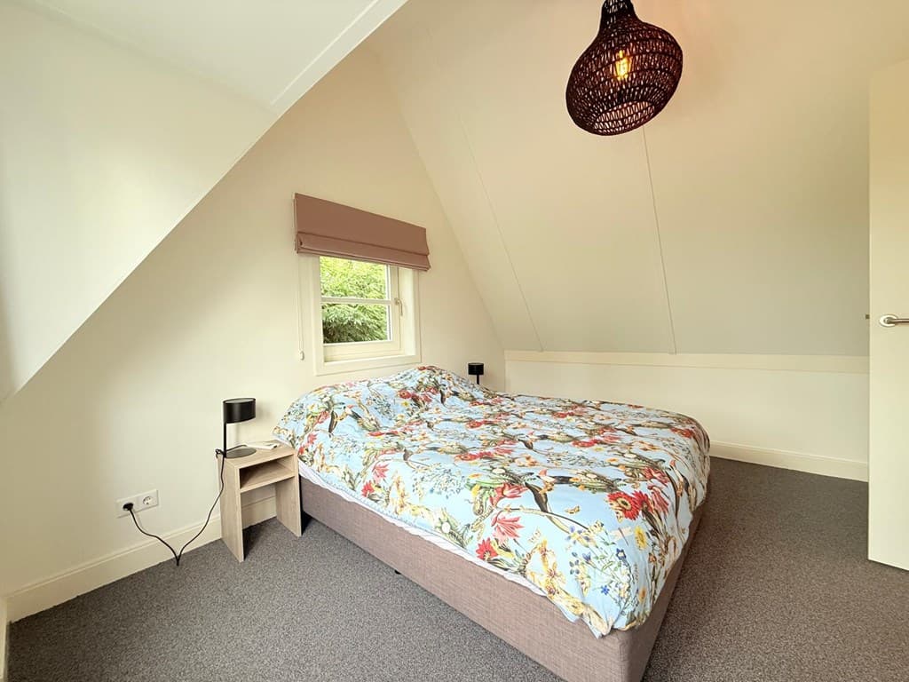 Slaapkamer met een tweepersoonsbed, kenmerkend bloemenbeddengoed en een sfeerlicht aan het plafond