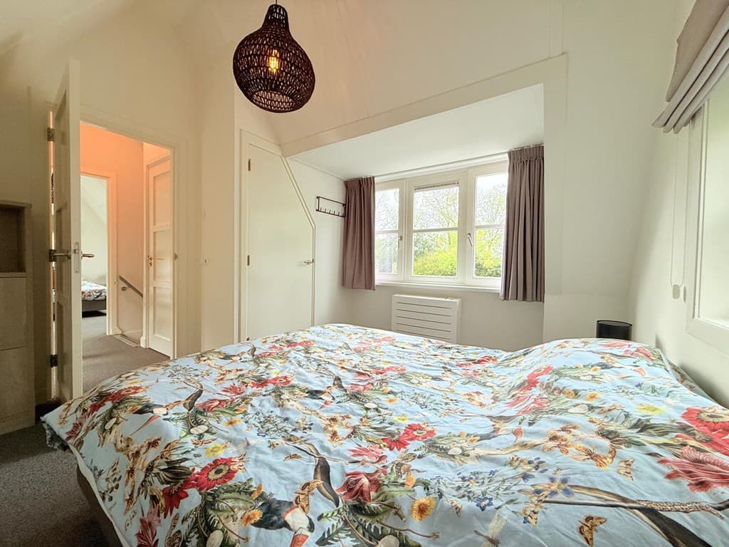 Slaapkamer met tweepersoonsbed, grote ramen en een sfeervolle lamp aan het plafond.