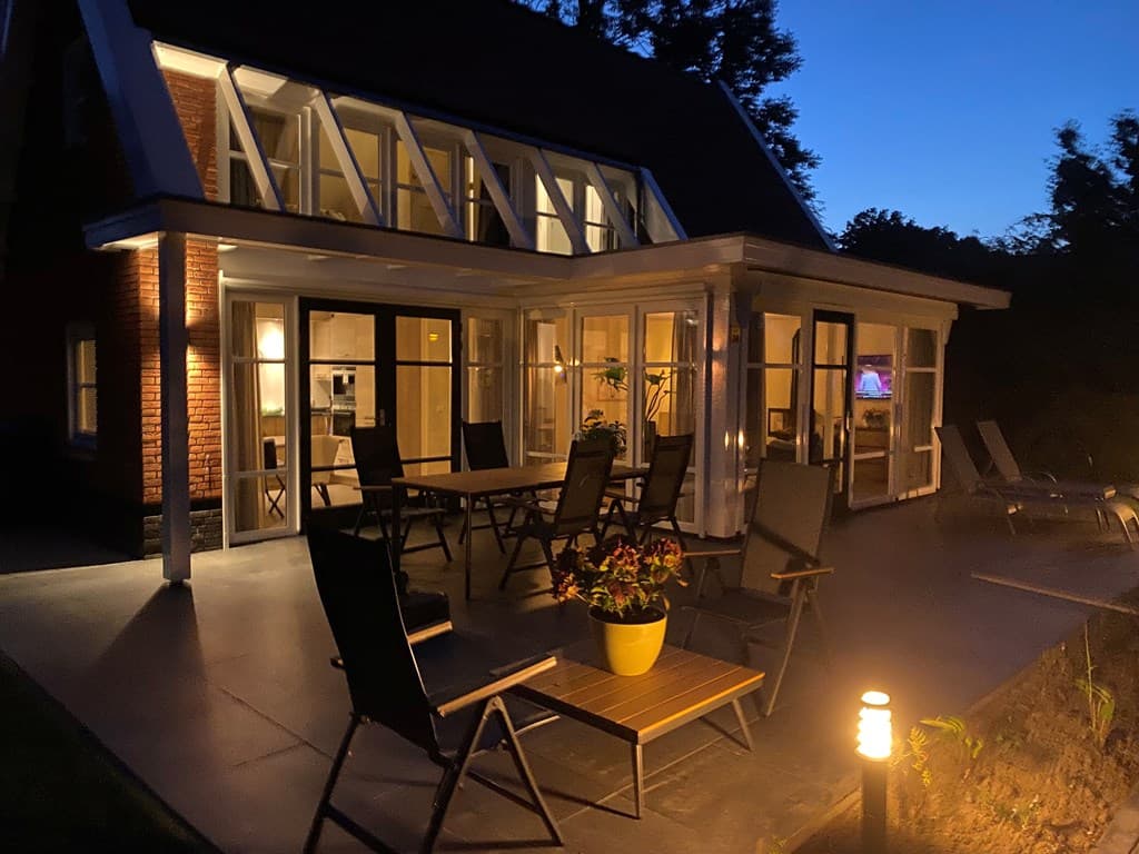 Buitenzijde van een vakantiewoning met een terras, verlichting en tuinmeubilair bij nacht.