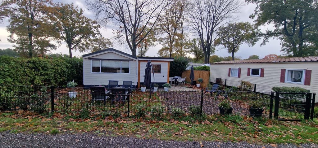 Buitenzicht van een vakantiewoning met terras, tuinset en omheining, omringd door groen en bomen