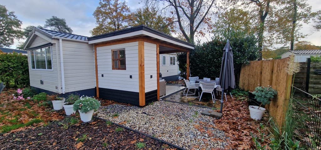 Vakantiewoning met houten accenten, terras, tuinmeubilair en een betegeld pad, omringd door bomen en planten.