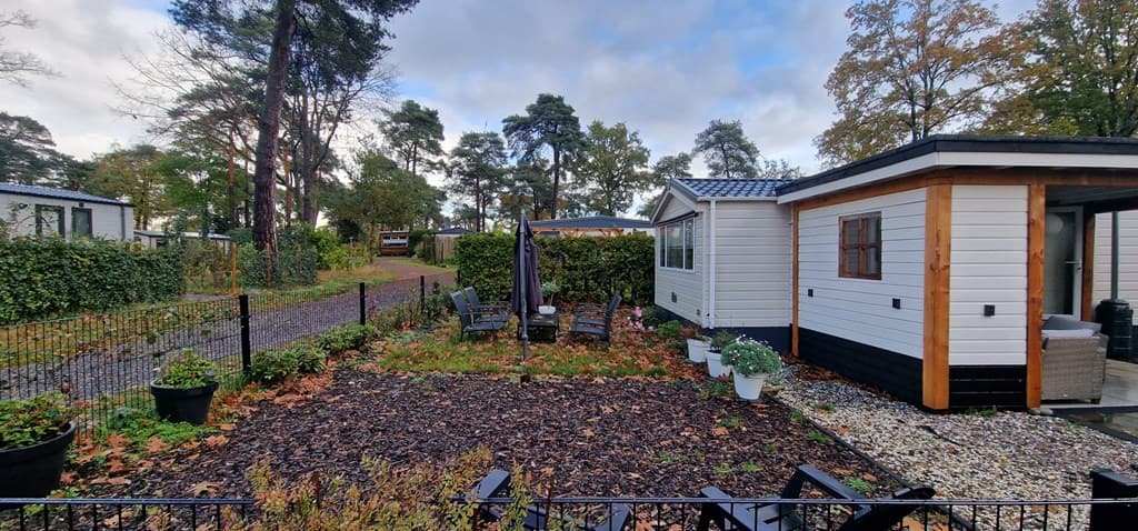 Tuin met terras en zitgelegenheid, omringd door bomen en gravelpaden bij een vakantiewoning.