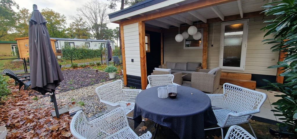 Terras met een houten vloer, een tafel met stoelen, en een zithoek met banken en verlichting, omgeven door groen.
