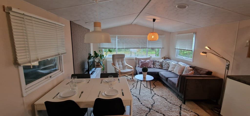 Interieur van een vakantiewoning met een zithoek, eettafel en grote ramen met veel lichtinval.
