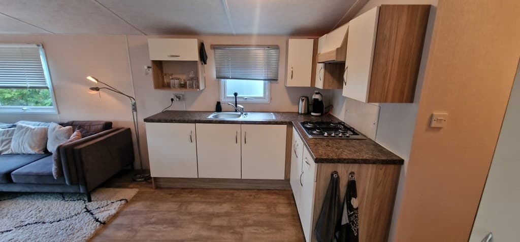 Keuken met lichte kasten, een wastafel, gasfornuis en een zithoek met een bank in de woonkamer