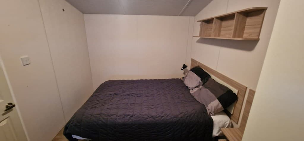Slaapkamer met een tweepersoonsbed, planken aan de muur en neutrale wandafwerking