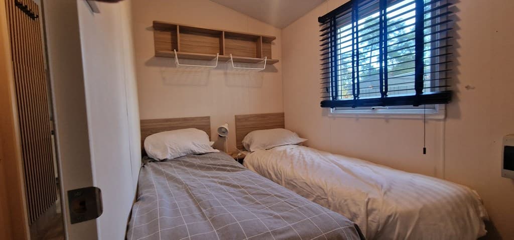 Slaapkamer met twee eenpersoonsbedden, wandplanken en een raam met jaloezieën