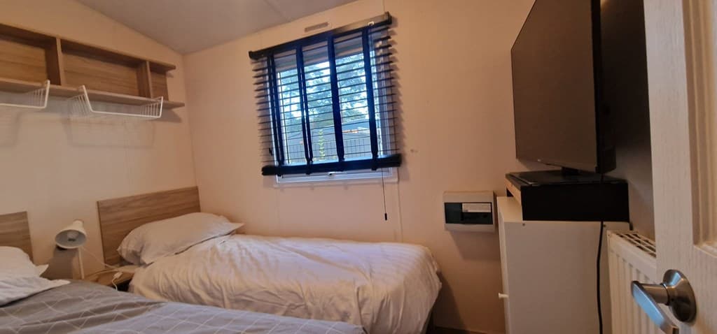 Slaapkamer met twee eenpersoonsbedden, venster met jaloezieën en een tv tegen de muur