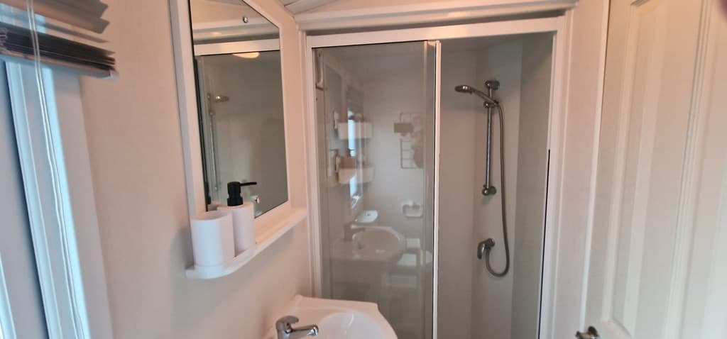 Badkamer met douchecabine, wastafel en spiegel in een lichte, moderne stijl.