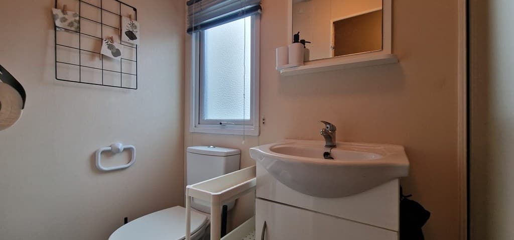 Toilet en wastafel met spiegel in een kleine badkamer, raam met kunststof kozijn en een handdoekhouder aan de muur