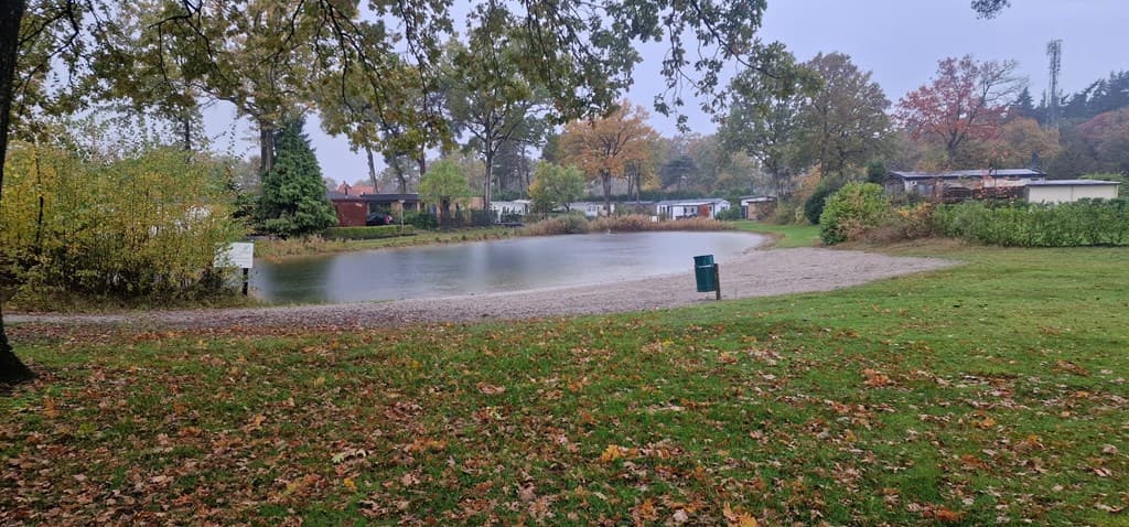 Uitzicht op een groene omgeving met een waterpartij, omringd door bomen en vakantiewoningen in een rustige setting