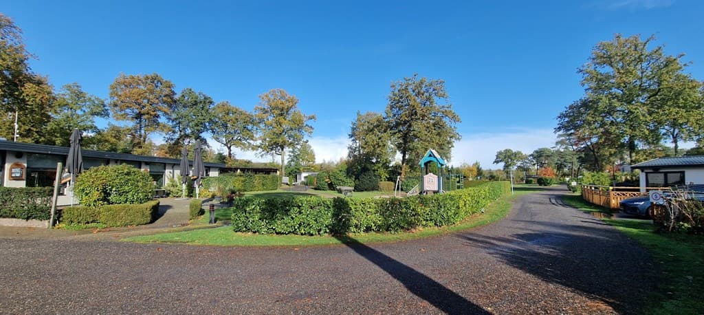 Uitzicht op het verblijfsterrein met bungalows, groene hagen en boomrijke omgeving onder een blauwe lucht.