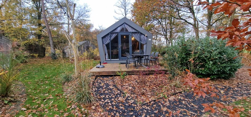 Moderne vakantiewoning met houten terras, omringd door bomen en struiken in een groene omgeving.