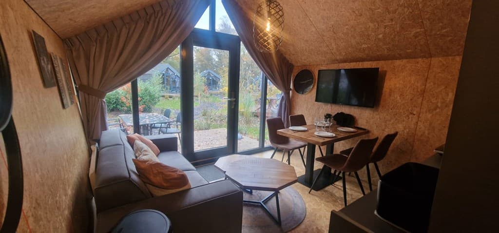 Gezellig interieur met zithoek, eettafel en grote ramen met uitzicht op de buitenruimte en natuurtuin