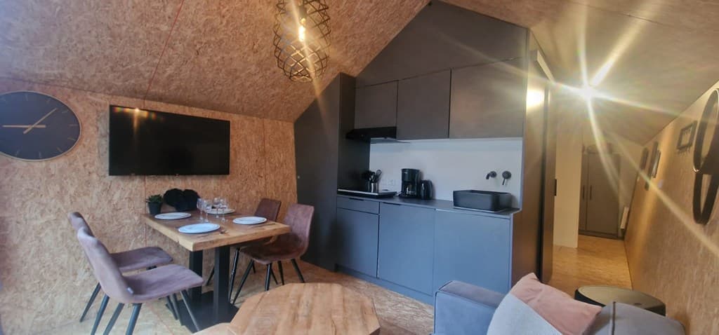 Gezellige woonkamer met open keuken, eettafel, moderne meubels en grote tv met wandklok aan de muur