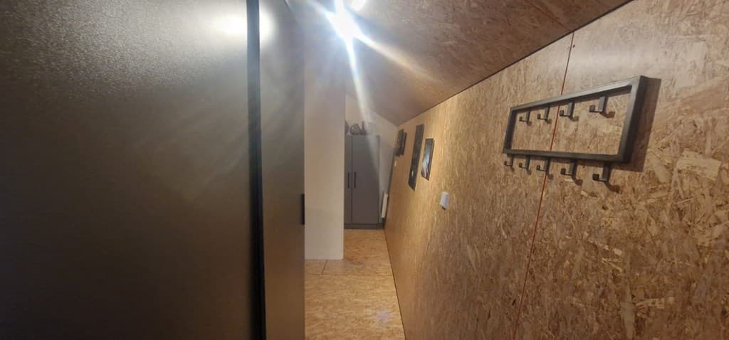 Smalle gang met houten wanden en een kapstok, zicht op een deur en kast aan het einde van de ruimte