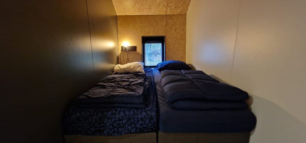 Tweepersoons slaapkamer met twee afzonderlijke bedden en een klein raam voor natuurlijk licht