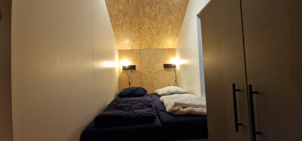 Slaapkamer met twee enkele bedden en wandlampen tegen een houten wand.