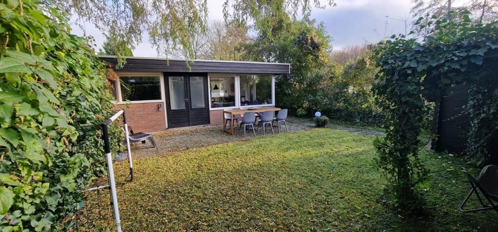 Vakantiehuis met ruime tuin, terras met tafel en stoelen, omgeven door groen en bomen.