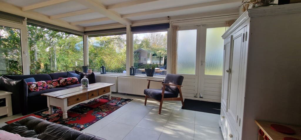 Lichte woonkamer met moderne meubels, een gezellige loungebank en een houten salontafel, uitzicht op de tuin.