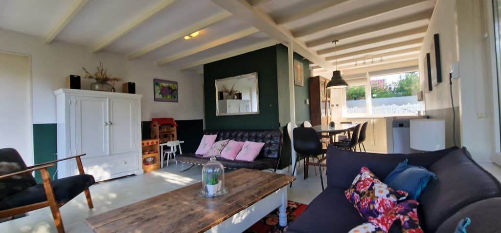 Woonkamer met banken, een houten tafel, decoratieve elementen en een open keuken met eettafel en stoelen.