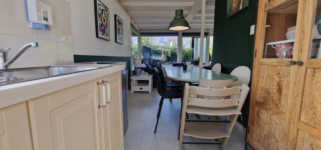 Een moderne open keuken met eettafel, stoelen en een houten kast, zicht op een groene tuin.