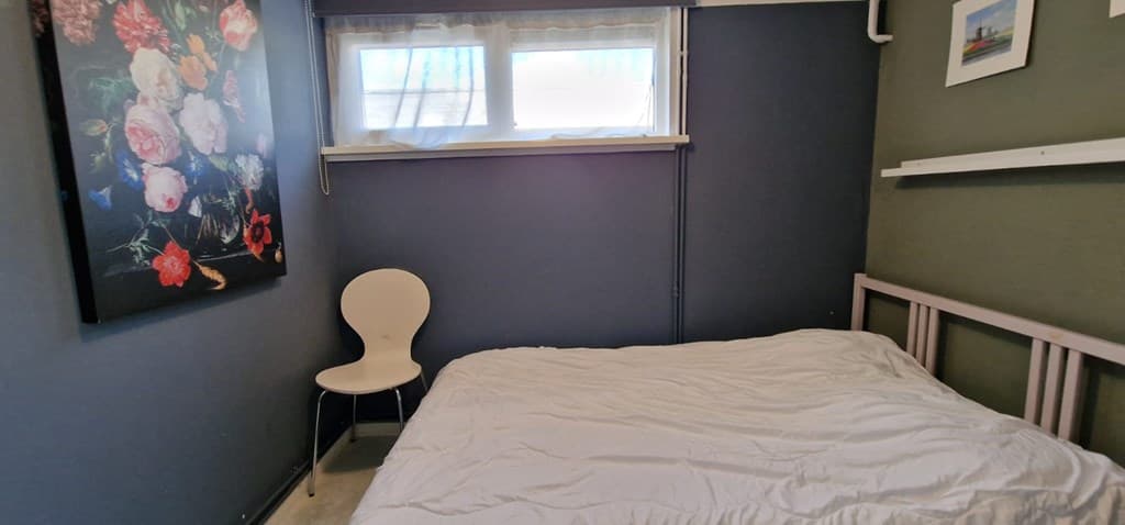 Slaapkamer met een bed, een witte stoel en een groot schilderij met bloemen aan de muur.