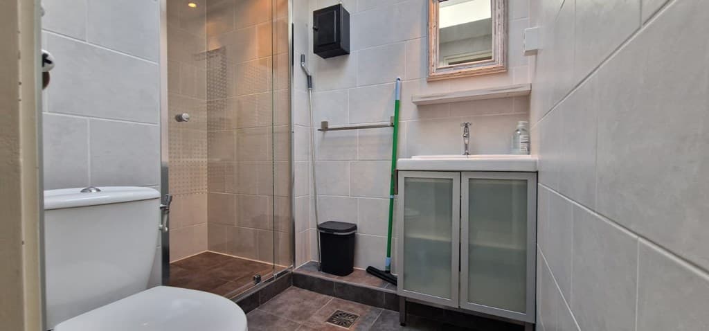 Moderne badkamer met toilet, douche, wastafel en opbergruimte in kast. Lichtgekleurde betegeling en praktische indeling.