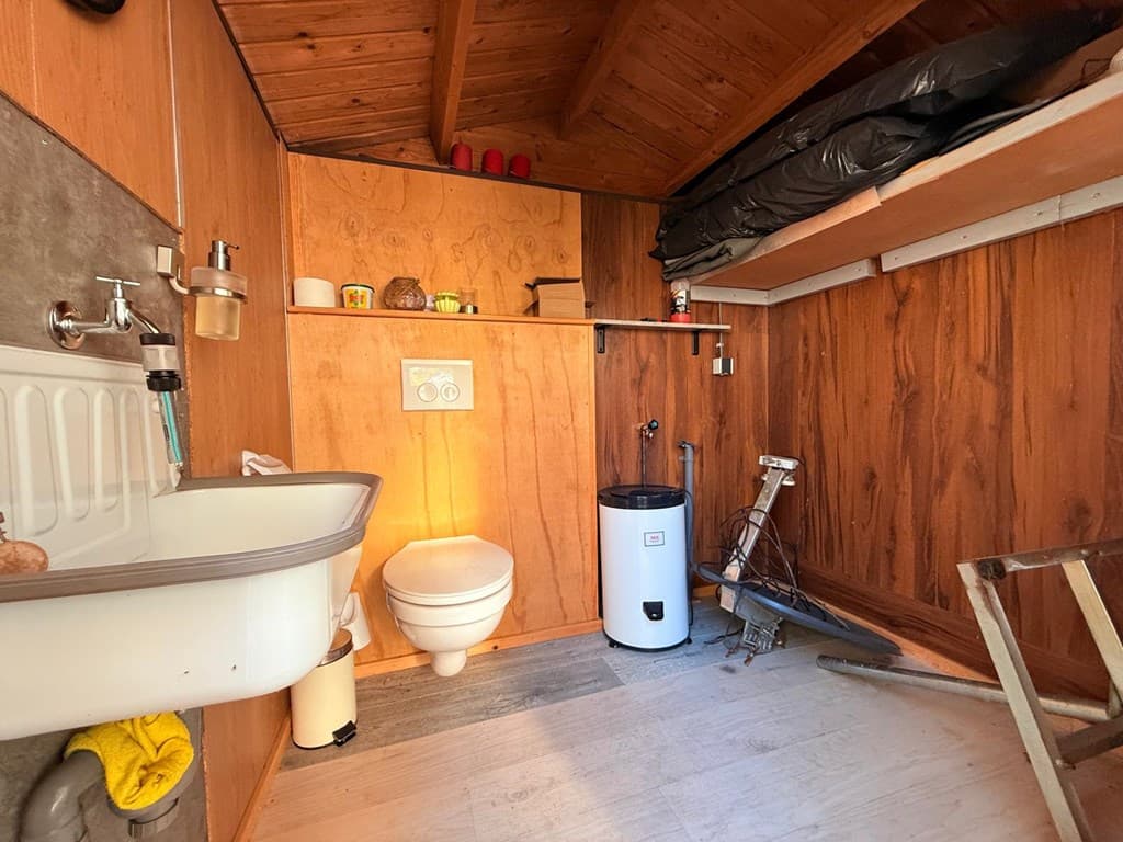 Hoek van een eenvoudige badkamer met toilet, wastafel en houten wanden in een vakantiewoning