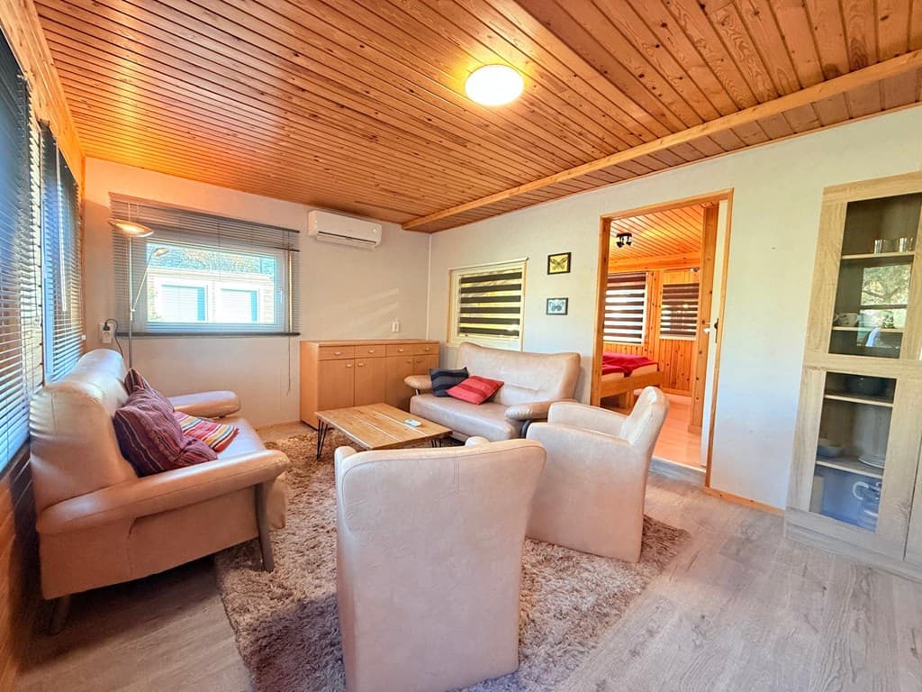 Zitkamer met houten plafond, bankstellen, een salontafel en kasten, naast een raam met zicht naar buiten.