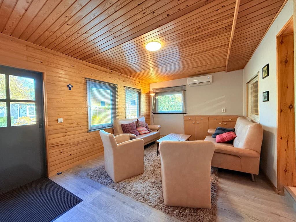 Woonkamer met houten plafond, meubels in neutrale kleuren en ramen met uitzicht op buiten.