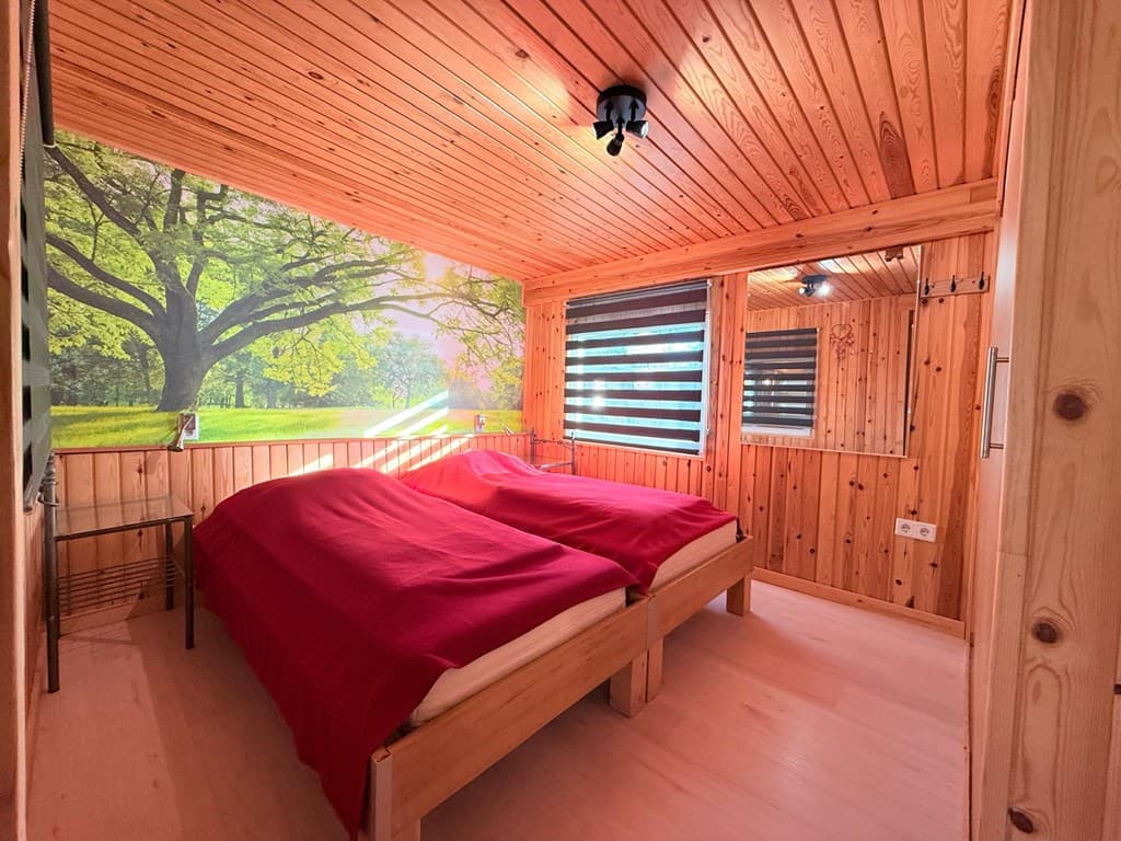 Sfeervolle slaapkamer met houten wanden, twee eenpersoonsbedden en uitzicht op een groene boom via een muurschildering