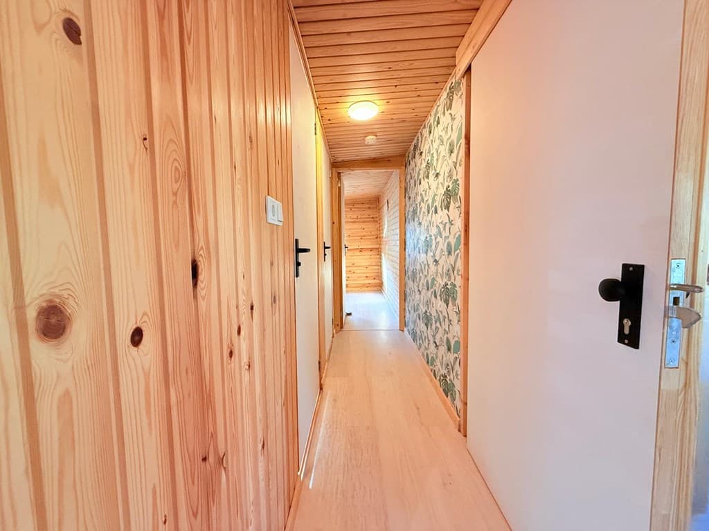 Houten gang met een plafond van houten planken en een muur met groene bloemenprint aan het einde van de gang