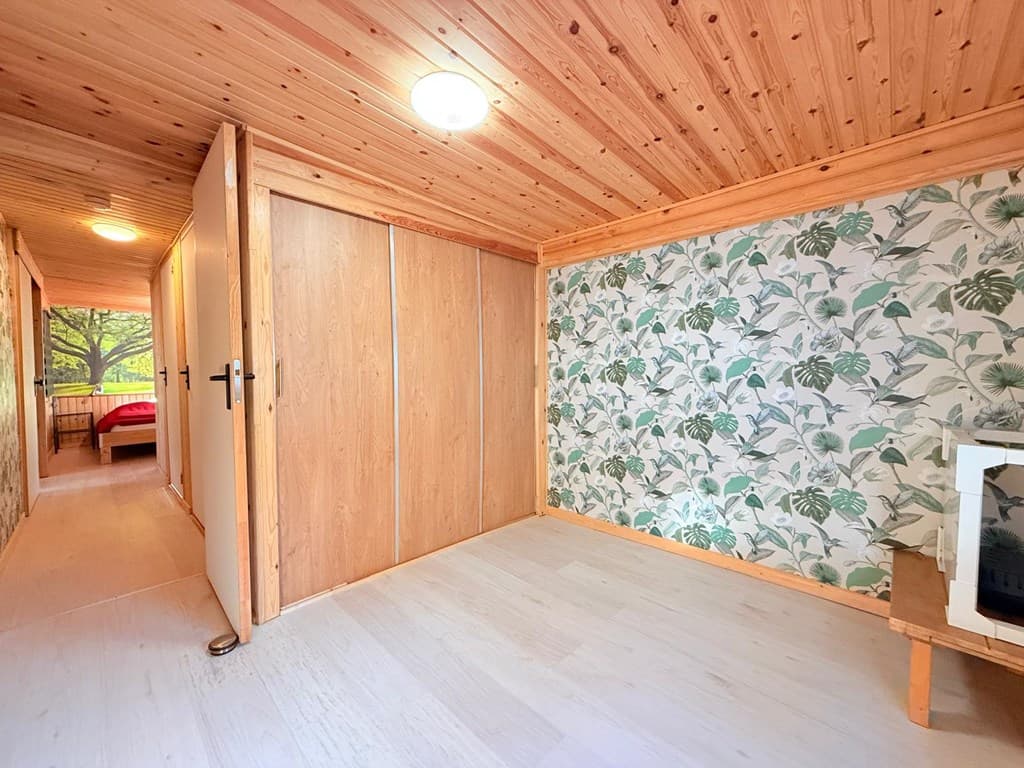 Interieur van een kamer met houten plafond, wanddecoratie met bladeren, en een kast in een vakantiewoning.