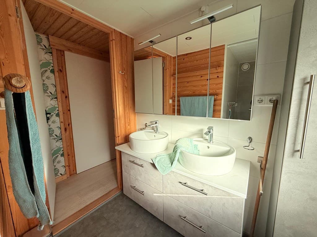 Moderne badkamer met dubbele wastafel, grote spiegels en houten accenten in een lichte ruimte