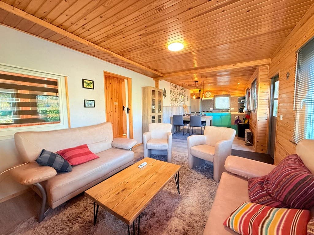 Gezellige woonkamer met houten plafond, zithoek en eethoek met een groene keuken op de achtergrond