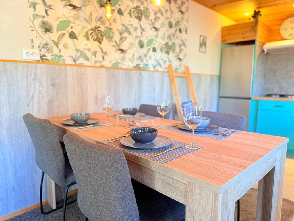 Eettafel met vier stoelen, gedekte tafel met borden en glazen, overzicht van een moderne woonkamer met plantenwanddecoratie