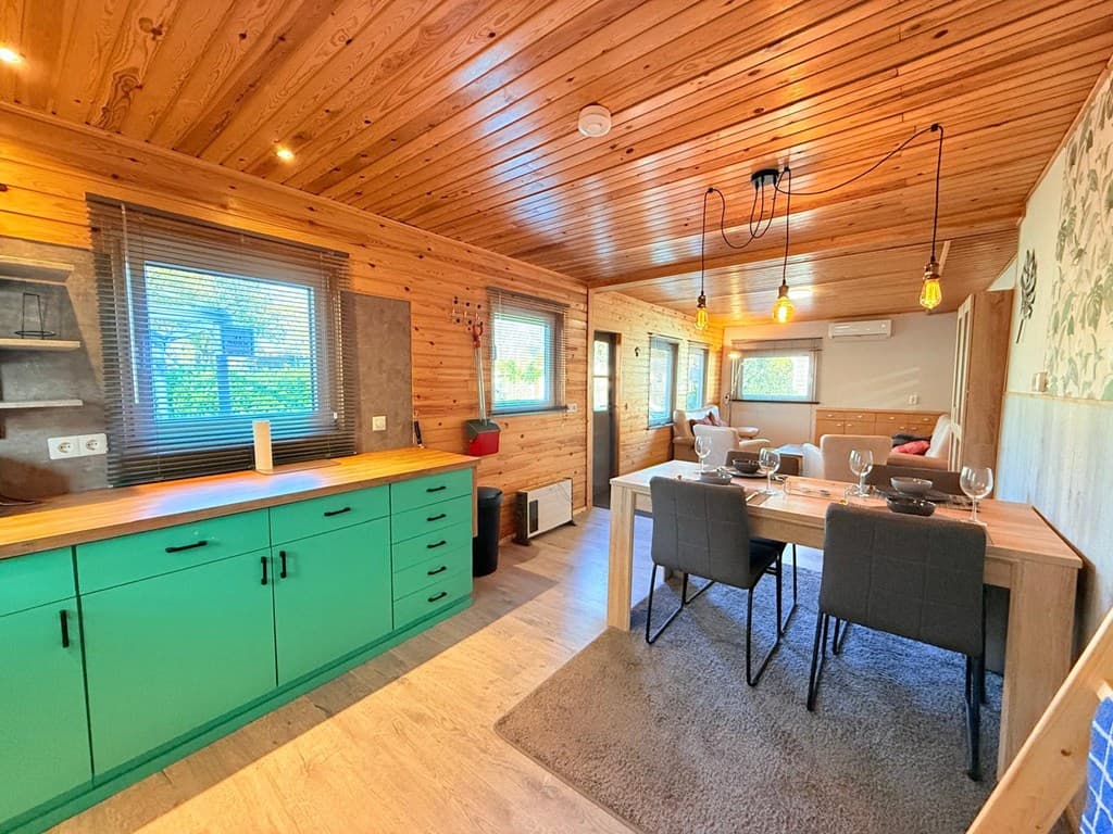Moderne woonruimte met houten plafonds, een groene kast, eettafel en grote ramen met uitzicht op buiten.