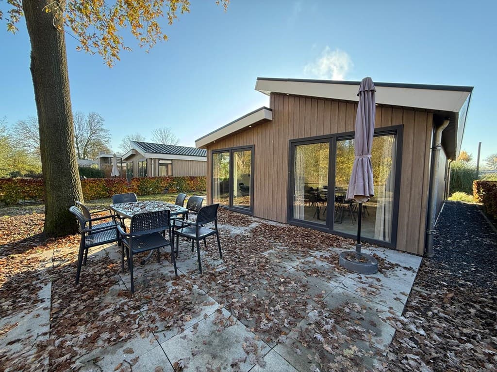 Moderne vakantiewoning met grote ramen, een terras en tafel met stoelen omgeven door herfstbladeren en bomen