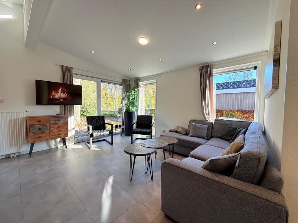 Zithoek met moderne meubels, grote ramen en een tv aan de muur in lichte woonkamer met tegenvloer