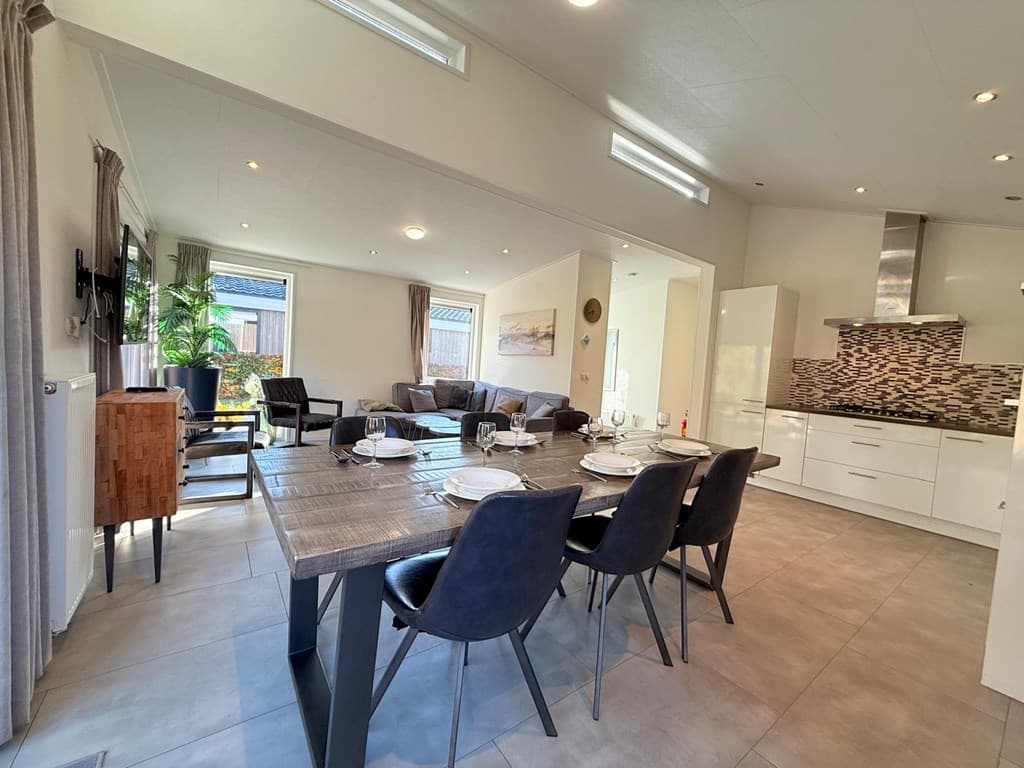 Ruim interieur van een vakantiewoning met eet- en zitgedeelte, grote tafel en moderne keuken met tegelvloer.