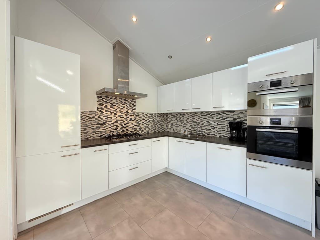 Moderne keuken met witte kasten, zwart aanrechtblad en betegelde achterwand in grijstinten.
