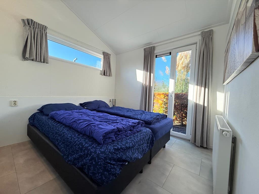 Slaapkamer met twee eenpersoonsbedden en toegang tot een terras via glazen deur met gordijnen aan de ramen