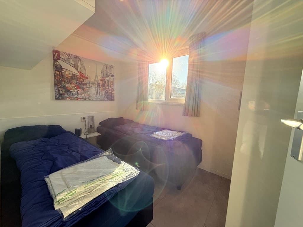 Slaapkamer met twee bedden, een raam met zonlicht en een schilderij aan de muur